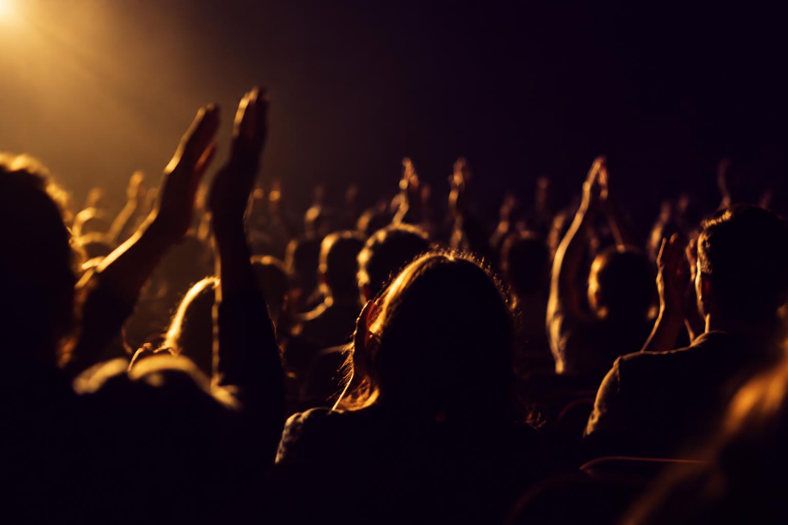 An audience applauding in a darkened theater, lit from the stage